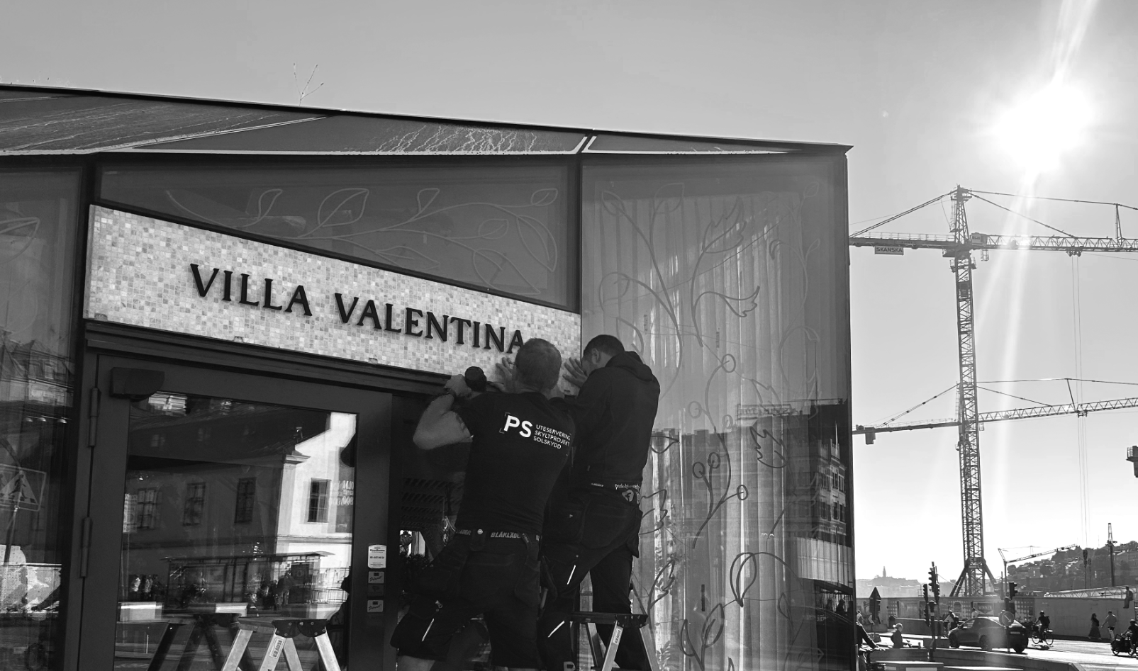 Två montörer från PS monterar skylten Villa Valentina på fasaden i motljus